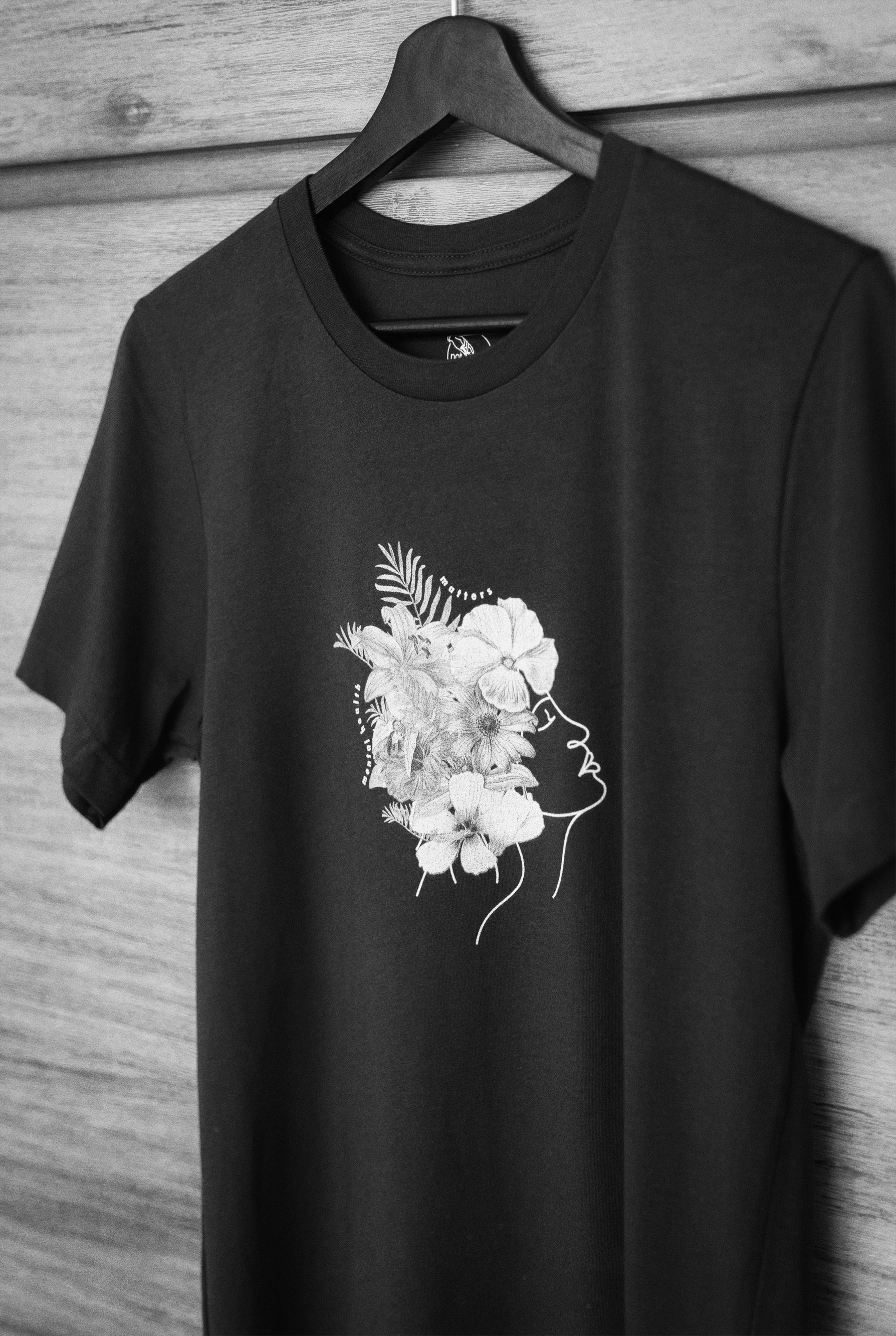 Close up image of Not Roses - Mental Health Matters T-Shirt. T-shirt is on a hanger against a timber background. 